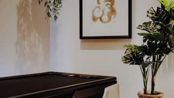 A billiards table with a 'VELUSJET medical' logo, a hanging plant, and framed artwork on the wall.