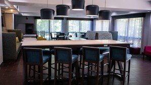 A modern dining area with a long table and multiple chairs, large windows with curtains, and a cozy seating area with a sofa and armchairs. - Hampton Inn Pickwick Dam-At Shiloh Falls (Counce)