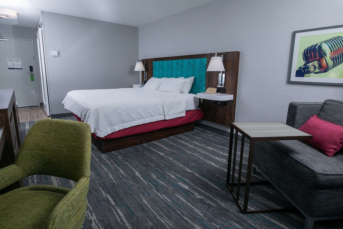 A hotel room with a bed, a desk, a chair, a sofa, and a painting on the wall.