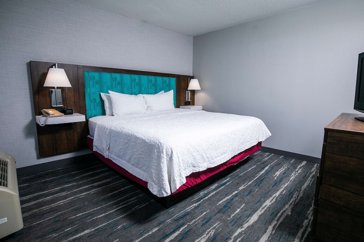 A hotel room with a large bed, two bedside tables, a TV, and a wall-mounted heater.