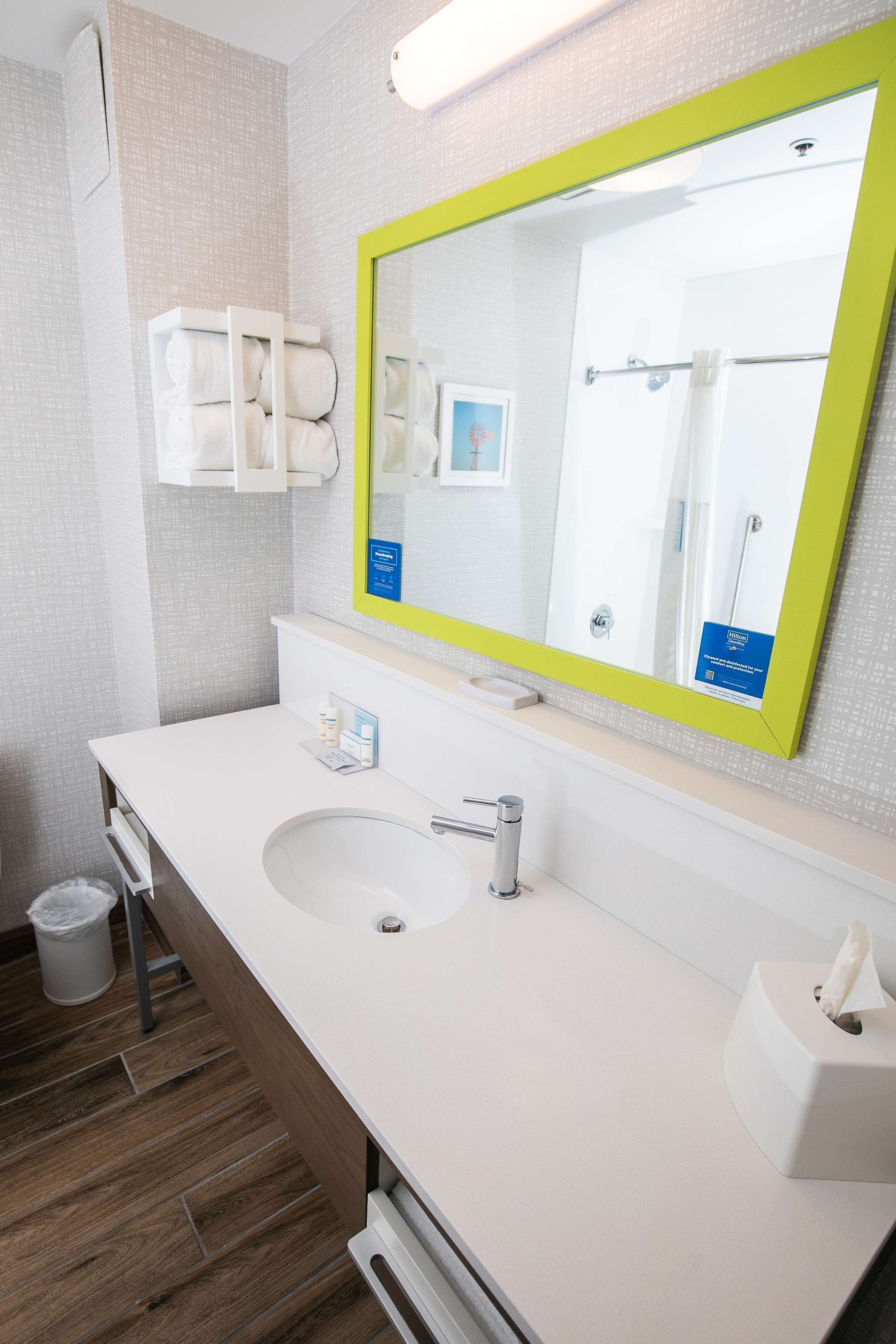 Un baño moderno con un lavamanos blanco, un espejo con marco verde y un toallero.