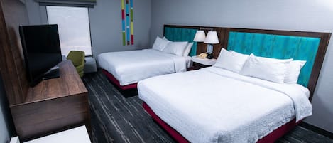 A hotel room with two beds, a TV, a desk, and a window.