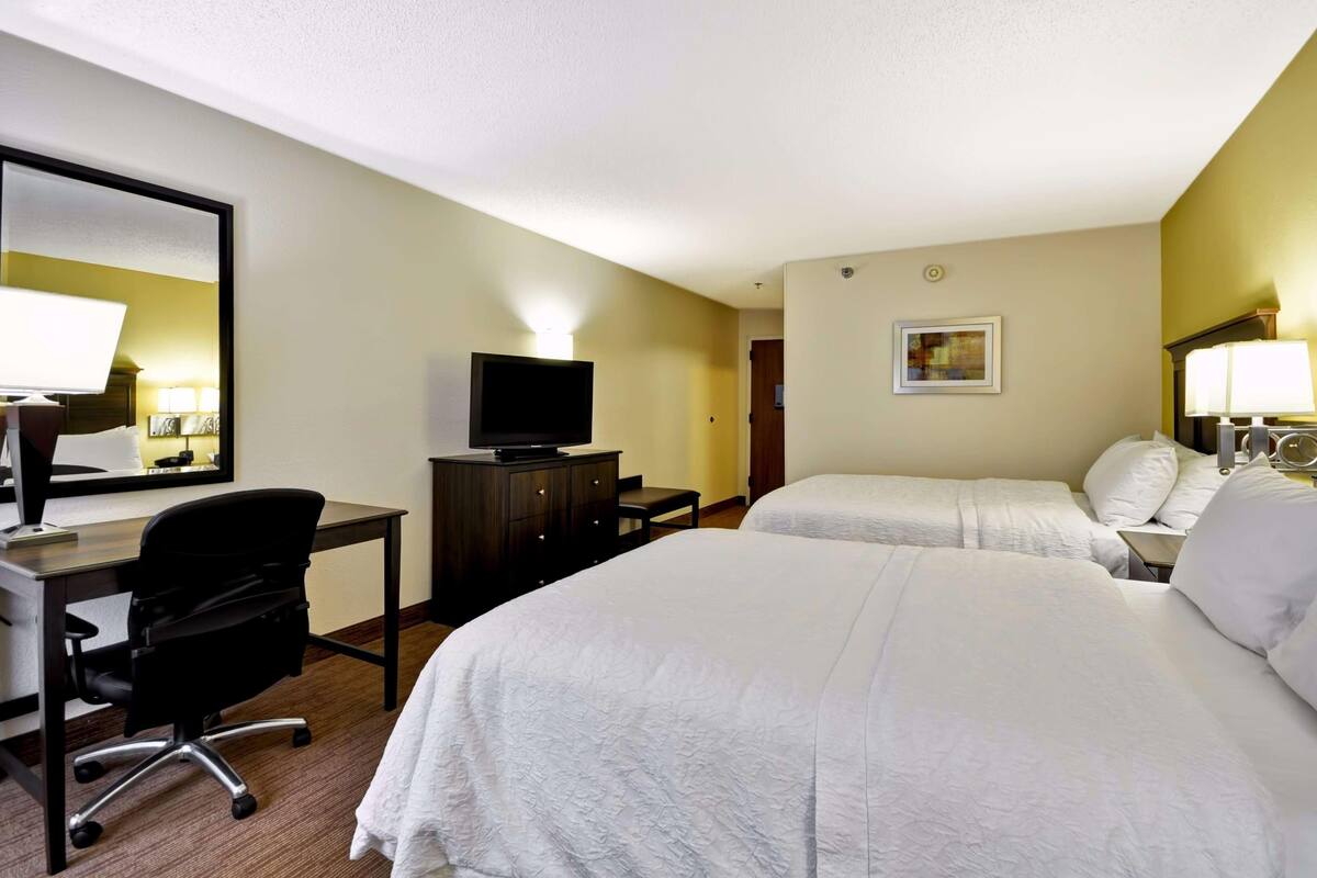 A hotel room with two beds, a desk with a chair, a television, and a mirror.
