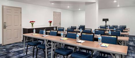 A conference room with multiple tables and chairs, equipped with water bottles and notepads.