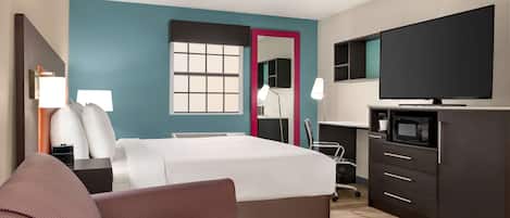 A hotel room with a bed, a TV, a desk with a lamp, and a microwave.