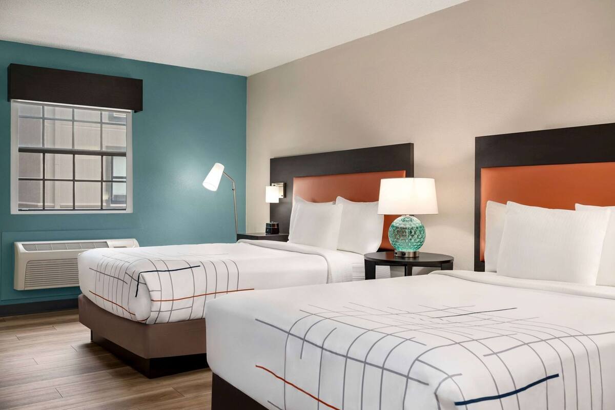 A hotel room with two beds, a window, a heater, a lamp, and a nightstand.