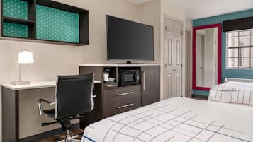 A hotel room with a bed, a desk with a chair, a television, a microwave, and a wardrobe.