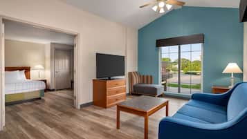 A hotel room with a bed, a TV, a sofa, a coffee table, a dresser, and a window with a view of greenery.