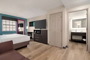 A hotel room with a bed, a desk with a flat-screen TV, a microwave, a wardrobe, and a bathroom with a sink and mirror. - La Quinta Inn by Wyndham Columbus I-70E/Reynoldsburg (Columbus)