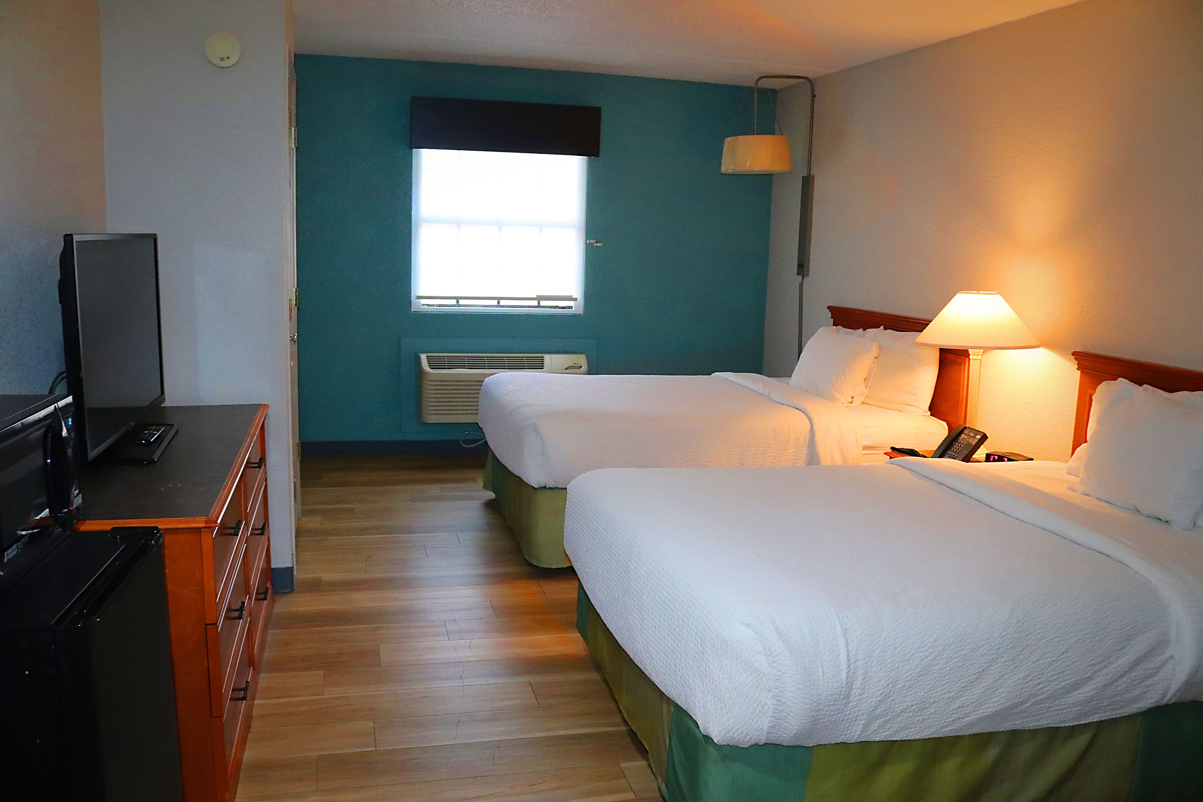 Una habitación de hotel con dos camas, un escritorio con televisor y una ventana con persianas.