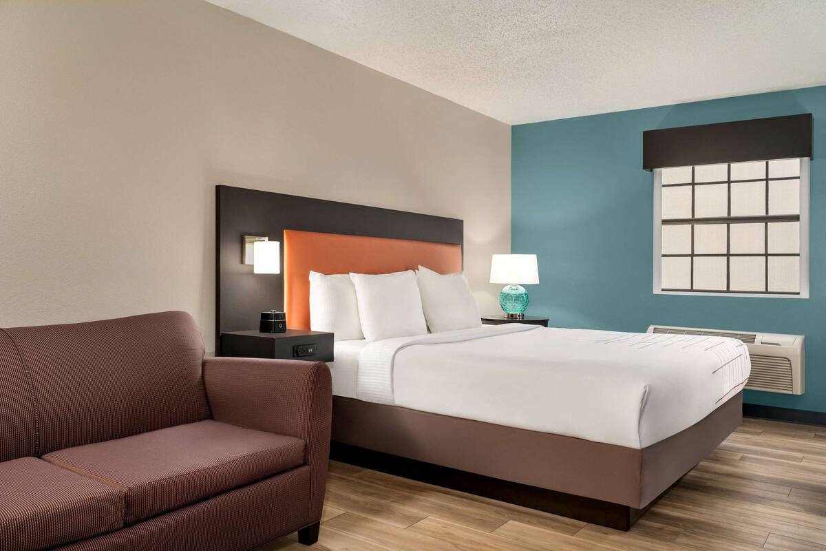 A hotel room with a bed, a nightstand, a lamp, a chair, and a window.