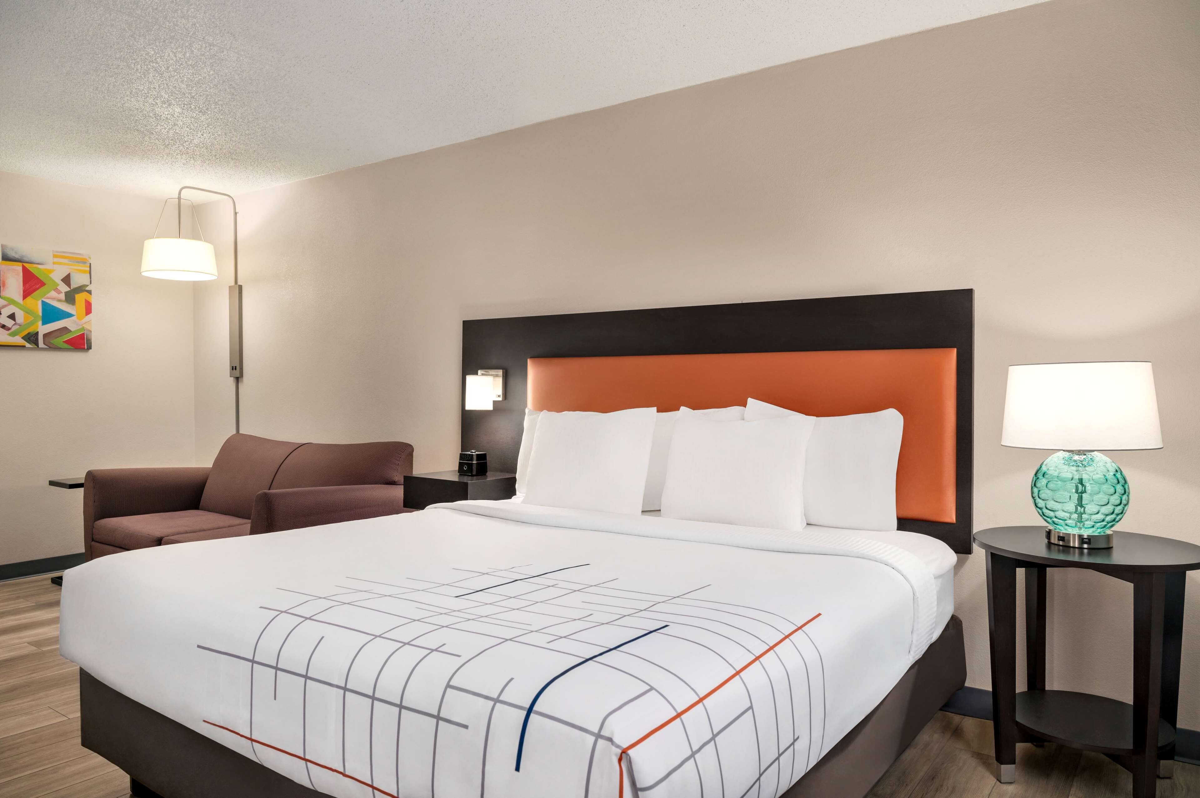 Une chambre d’hôtel avec un grand lit, un fauteuil brun, un bureau avec une lampe et un globe décoratif posé sur une table d’appoint.