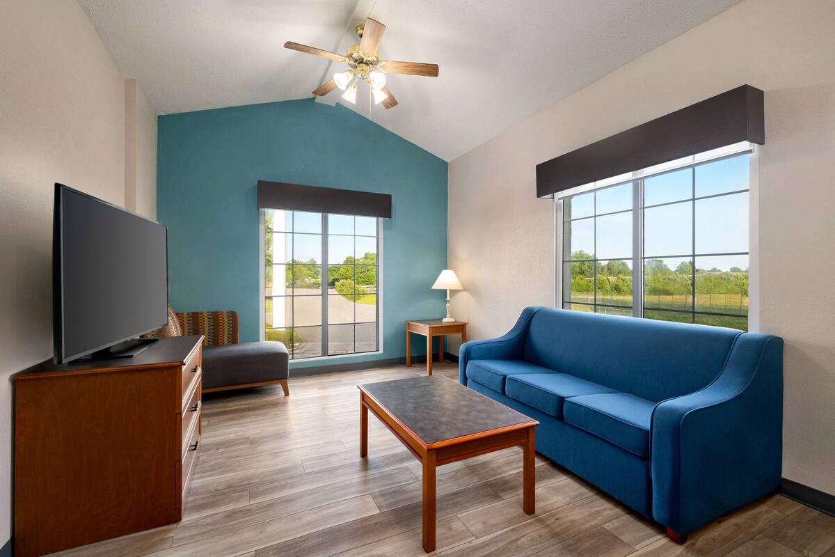 A modern living room with a blue couch, a flat-screen TV, a wooden coffee table, and a ceiling fan.