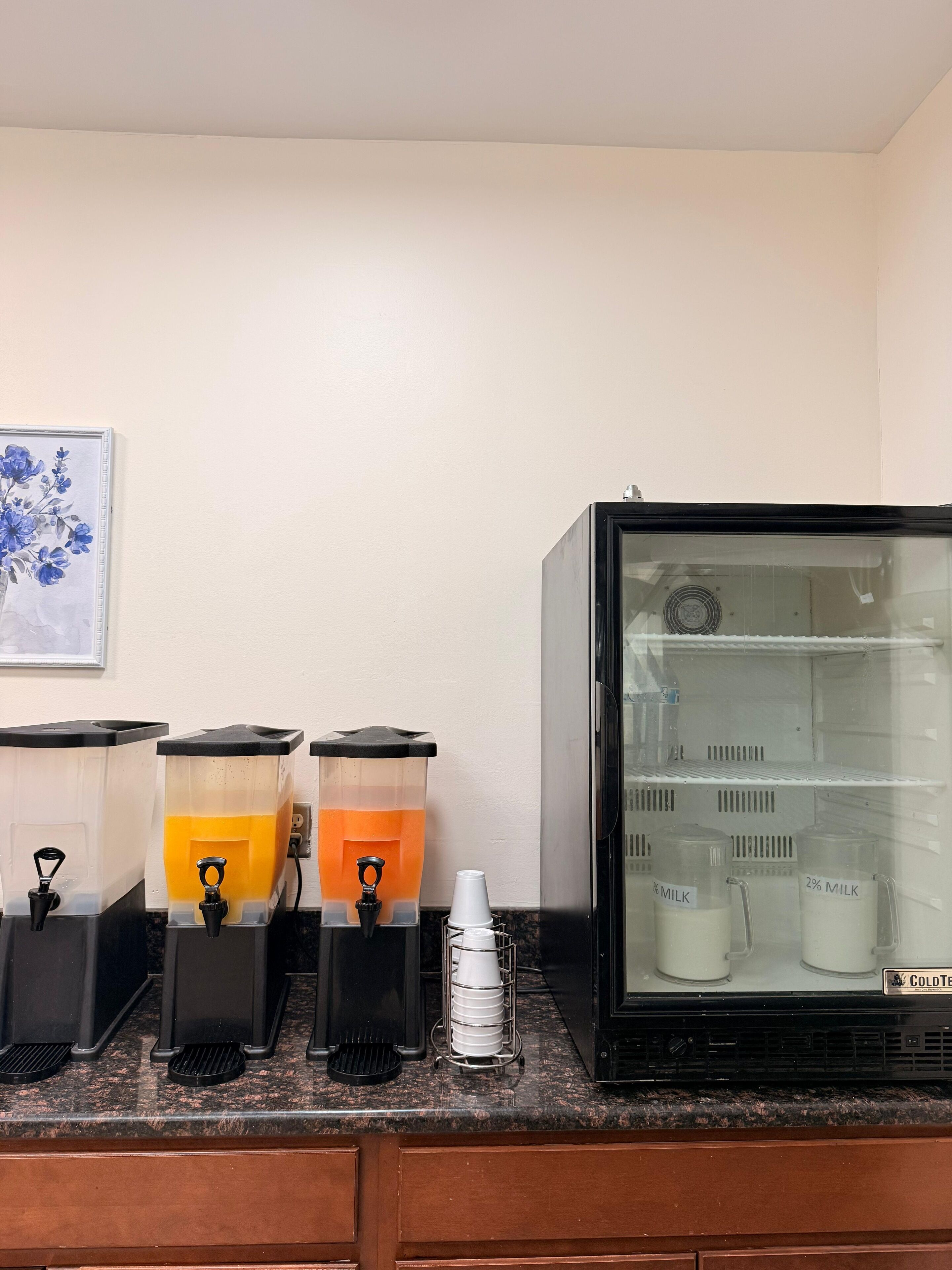 A beverage station with dispensers and a refrigerator stocked with milk.