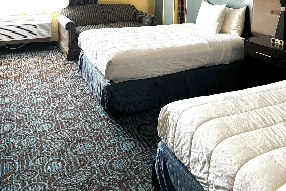 A hotel room with a bed, a chair, a bedside table with a lamp, and a large window with curtains.