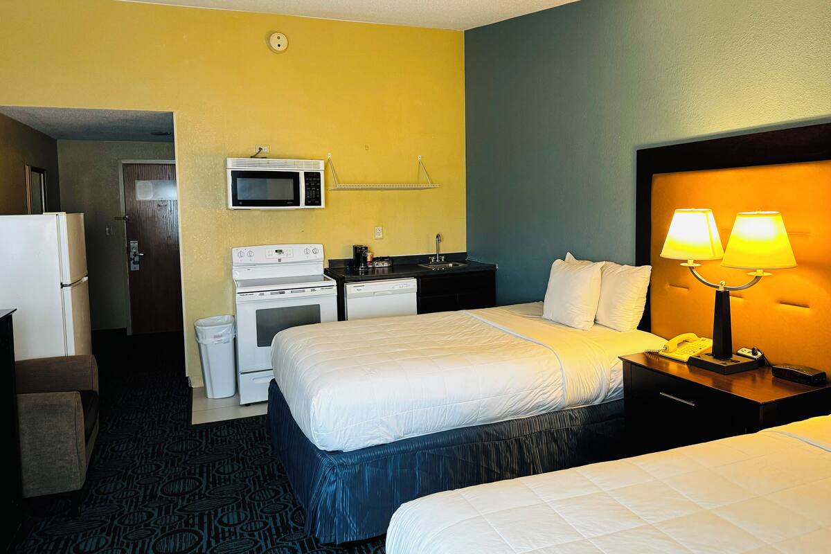 A hotel room with two beds, a microwave, a stove, a sink, and a telephone.