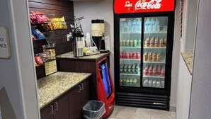 Un frigo Coca-Cola pieno di diverse bevande, una macchina per caffè e distributori automatici di snack in una stanza piccola.