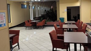 Un'area ristorazione di un hotel con diversi tavoli e sedie, un lampadario e una scala che conduce a un piano superiore.