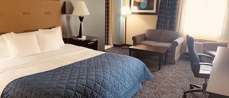 A hotel room with a large bed, a desk, a chair, and a lamp.