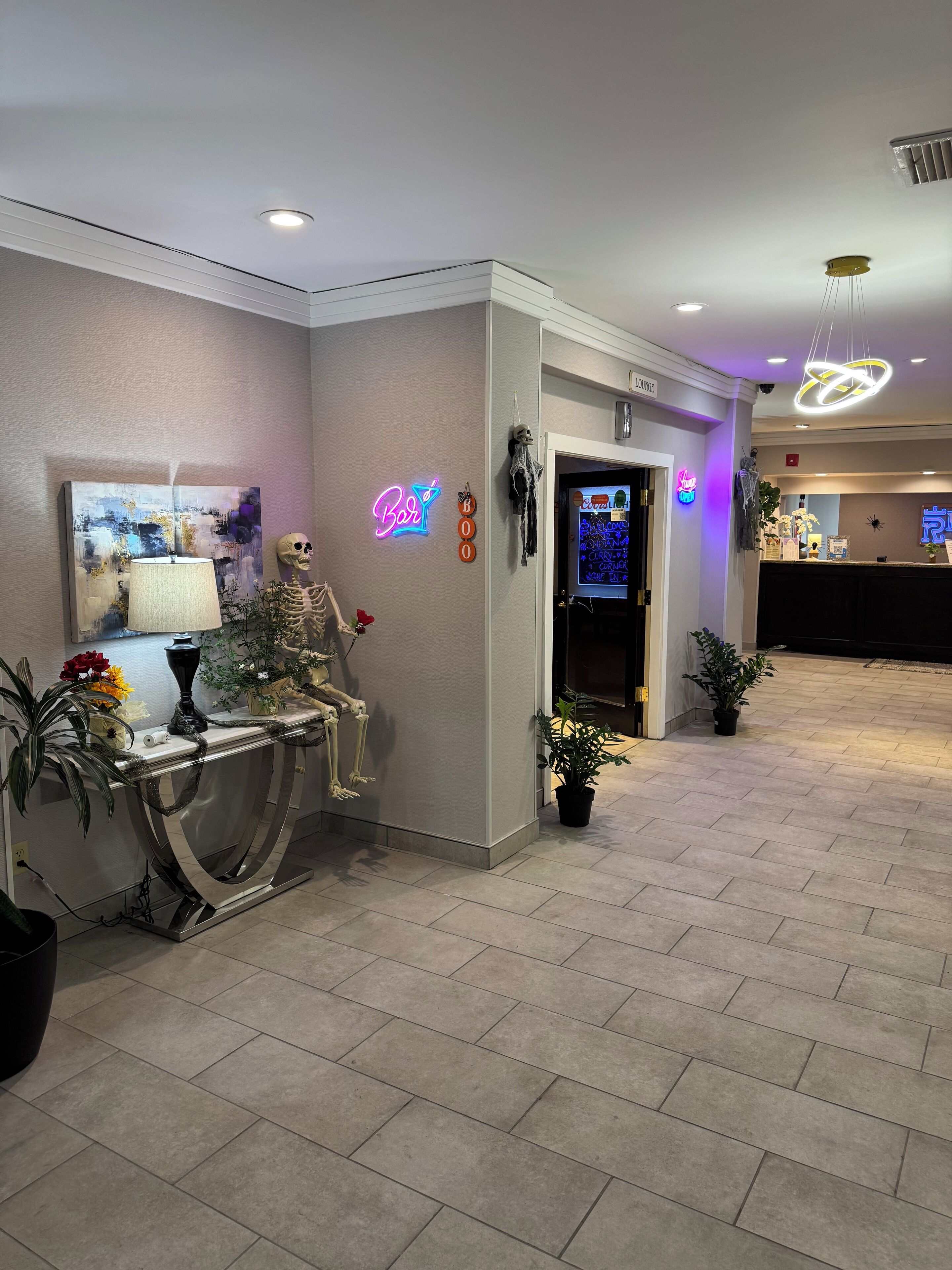Un vestíbulo de hotel con una recepción, un letrero de neón, una decoración de calavera y un cuadro en la pared.