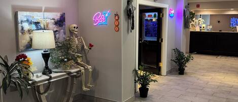 Un vestíbulo de hotel con una recepción, un letrero de neón, una decoración de calavera y un cuadro en la pared.