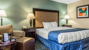 Una camera d'albergo con un letto grande, due comodini con lampade, una sedia e un tavolino con vassoio.