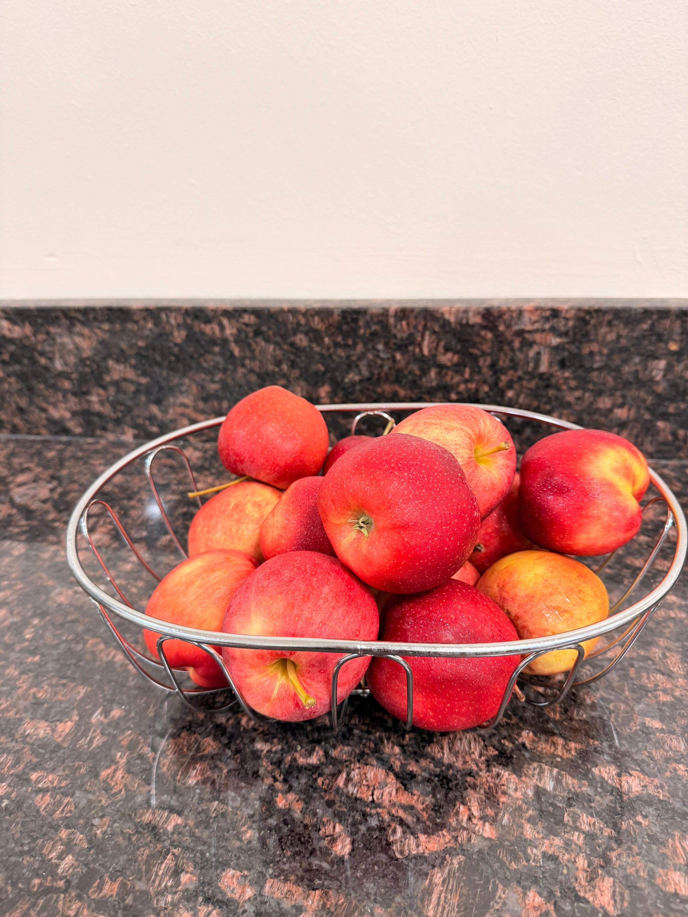 Una cesta de metal llena de manzanas rojas sobre una encimera de granito.