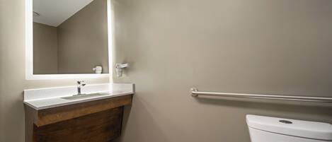 Un baño con tocador de madera, lavamanos blanco, espejo y retrete blanco.