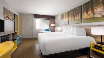 A hotel room with a bed, a desk, a chair, a TV, and artwork on the wall.