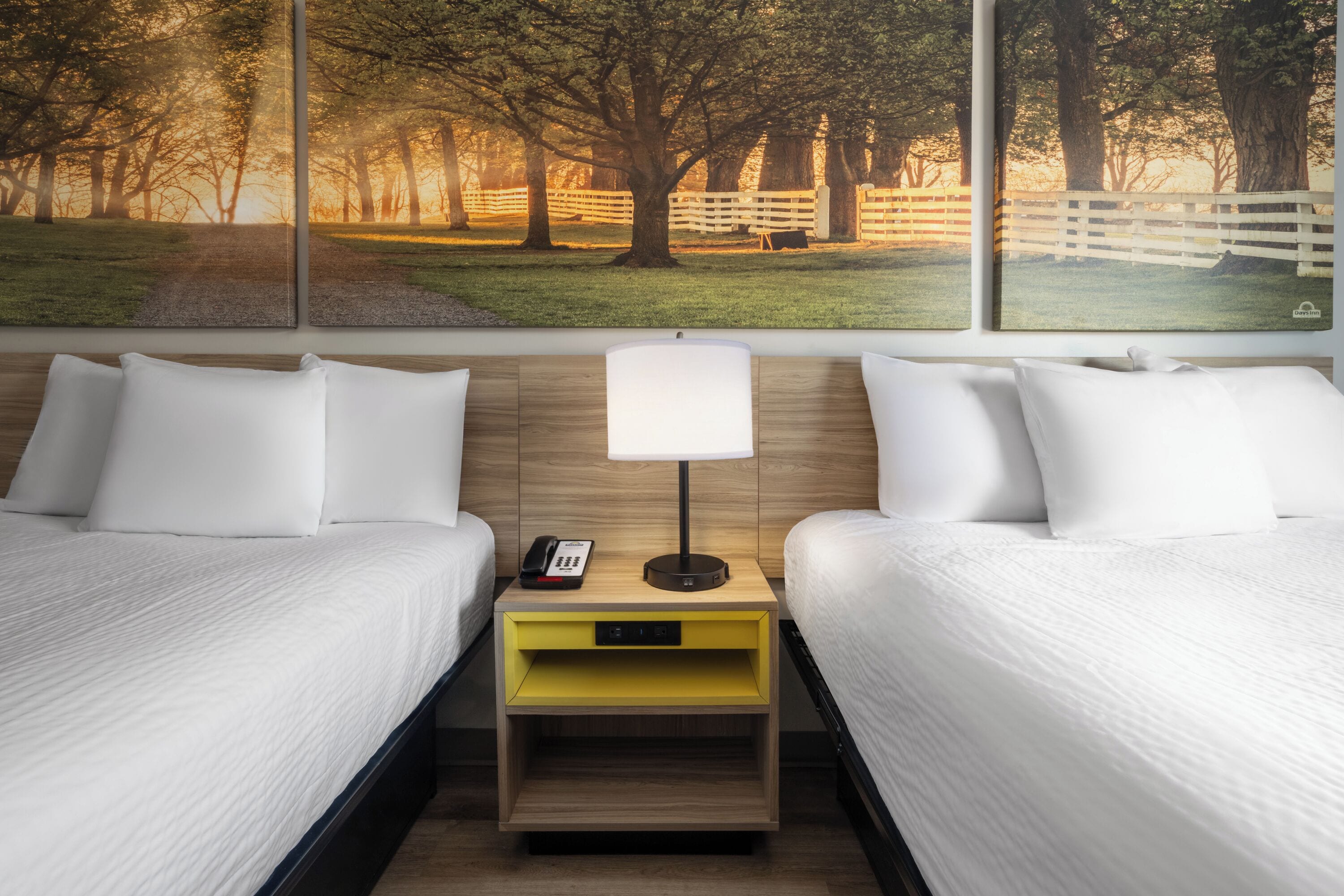 Habitación de hotel con dos camas, una mesita de noche con lámpara, teléfono y un cajón de almacenamiento amarillo.