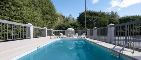 A swimming pool with white lounge chairs and a metal fence.