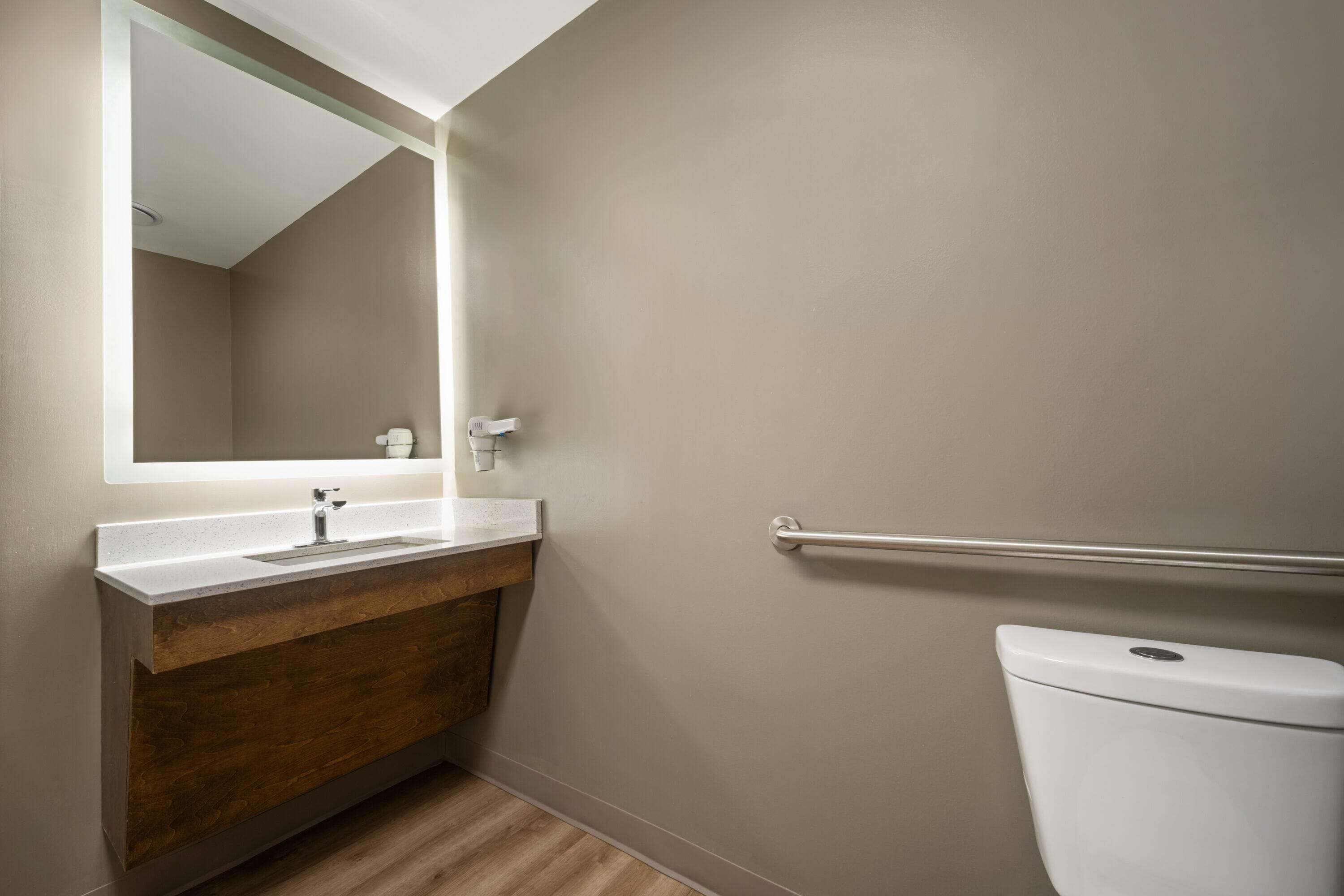 A bathroom with a wooden vanity, a white sink, a mirror, and a white toilet.