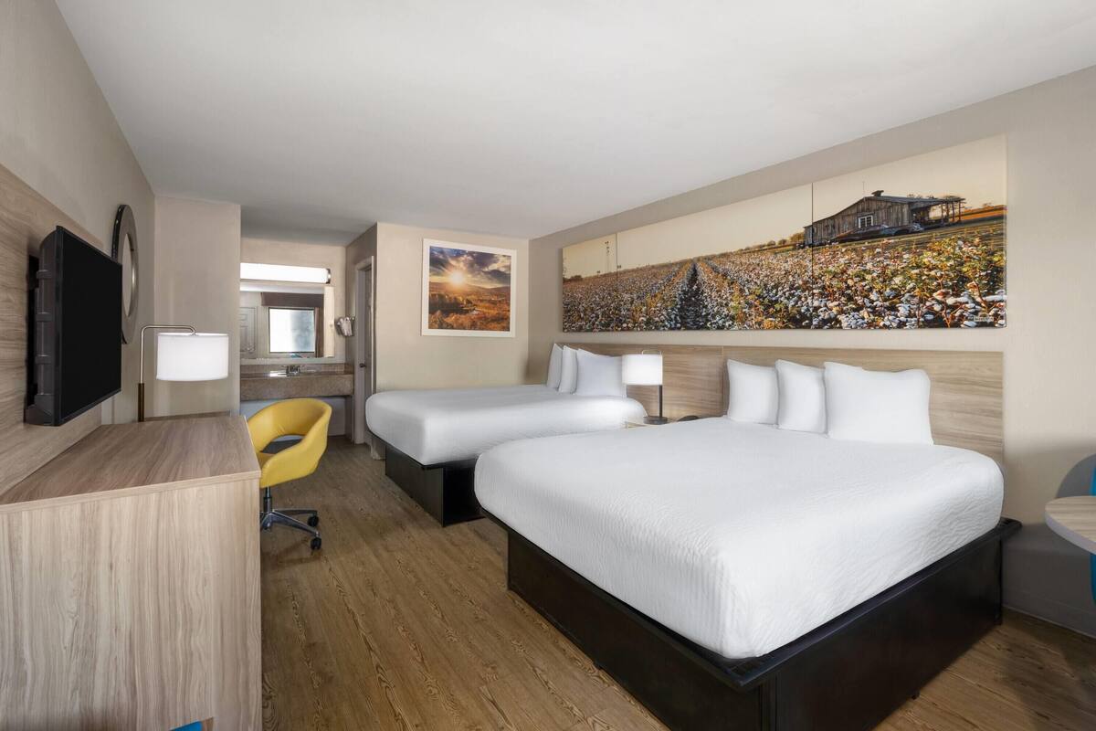 Habitació d'hotel amb dos llits, un escriptori, una cadira i un quadre gran a la paret.