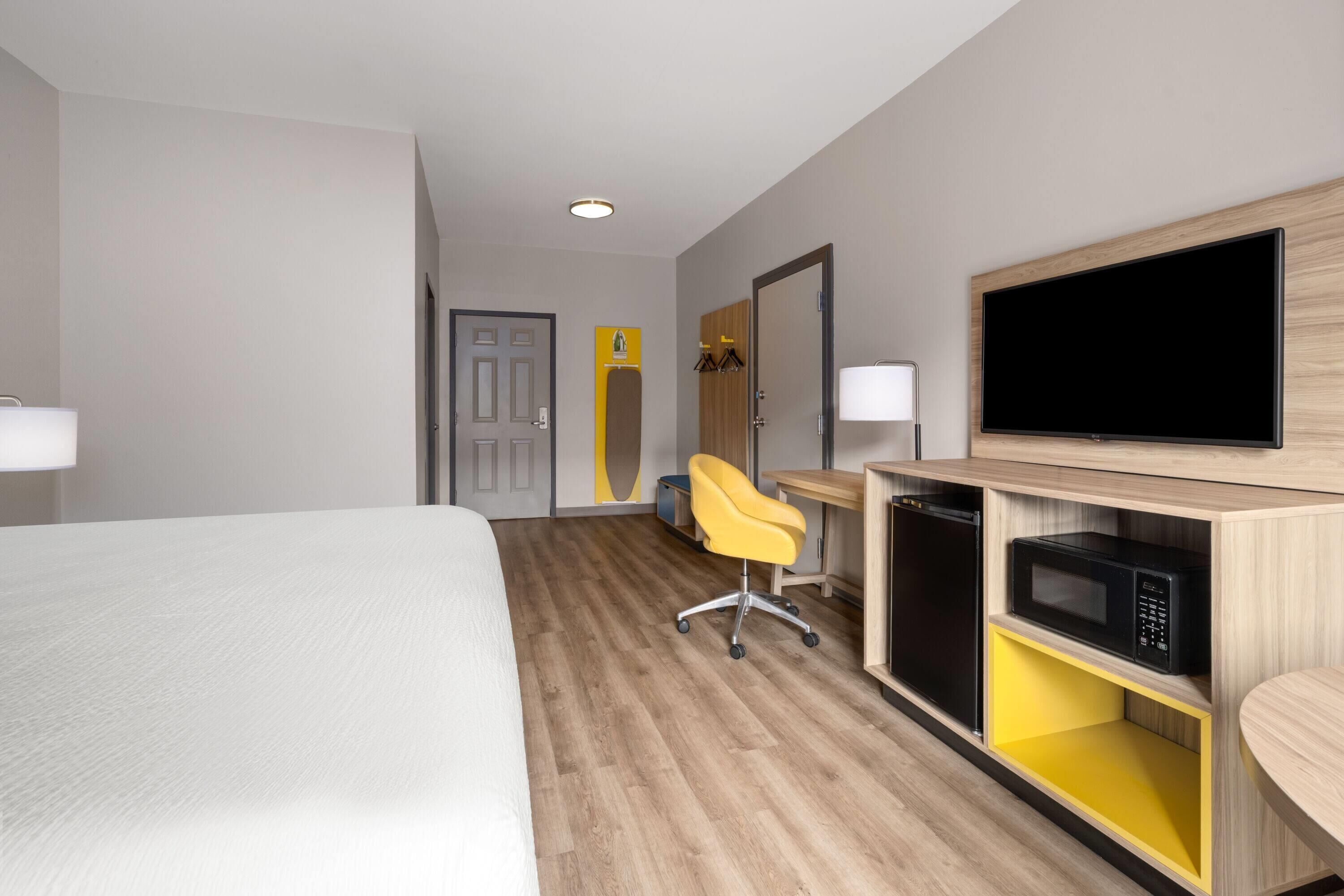 A hotel room with a bed, a desk with a flat-screen TV, a microwave, and a yellow chair.