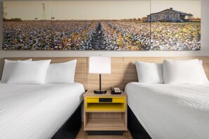 A hotel room with two beds, a nightstand with a lamp, and a large painting of a cotton field and barn.