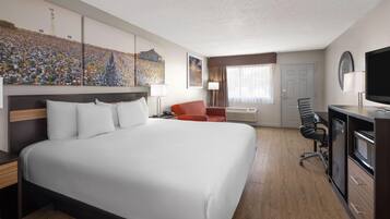 Habitación de hotel con una cama grande, un escritorio con computadora, una silla, un televisor y obras de arte en las paredes.