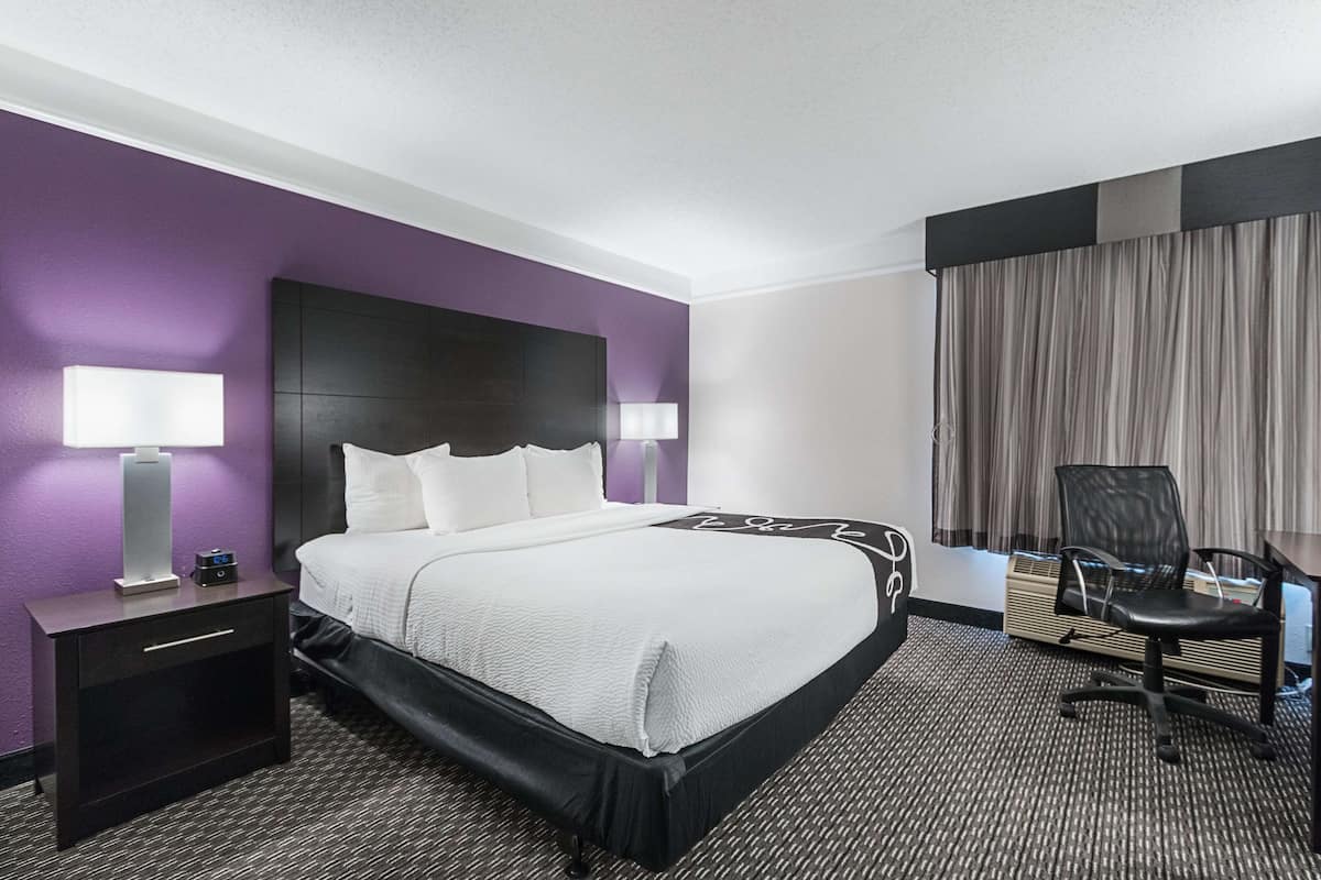 Une chambre d’hôtel avec un grand lit, deux tables de chevet avec des lampes, un bureau avec une chaise et une fenêtre avec des rideaux.