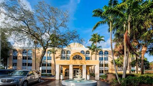 Een hotel met een fontein in het midden, palmbomen en een helderblauwe lucht.