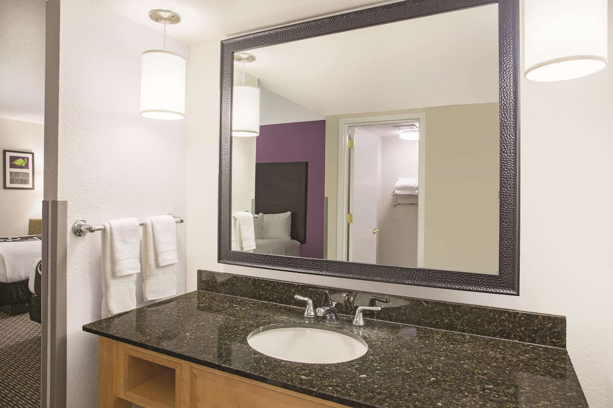 Une salle de bain avec un lavabo doté d’un plan de travail en granit, un grand miroir et un porte-serviettes avec des serviettes blanches.