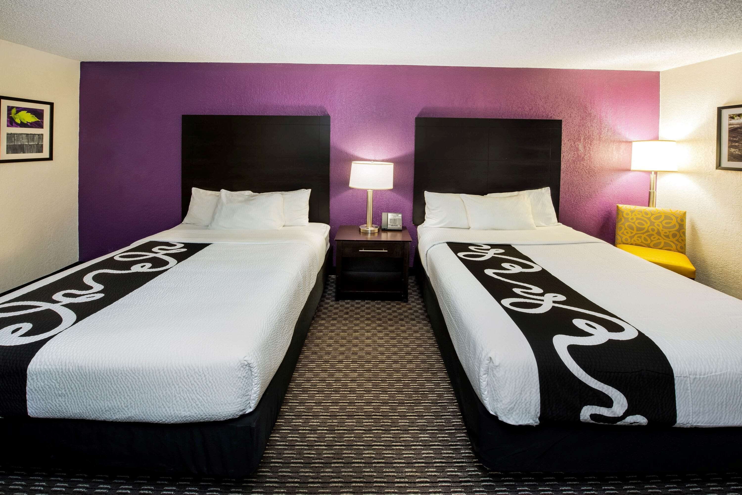 A hotel room with two beds, purple walls, and a patterned carpet.