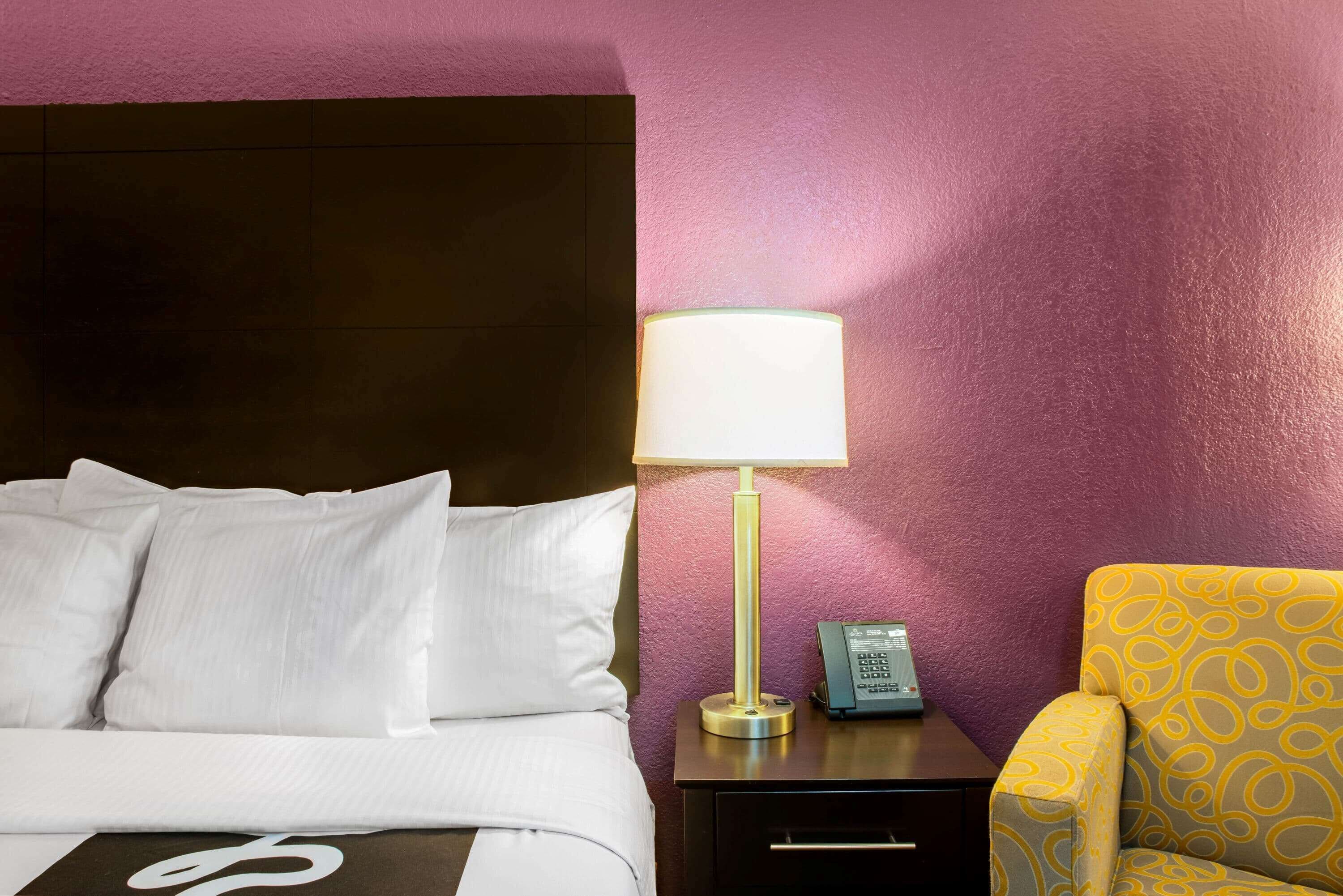 Une chambre d’hôtel comprenant un lit, une table de chevet, une lampe, un téléphone et un fauteuil à motifs.