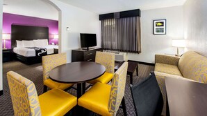 Een hotelkamer met een bed, een televisie, een eettafel met gele stoelen en een bank.