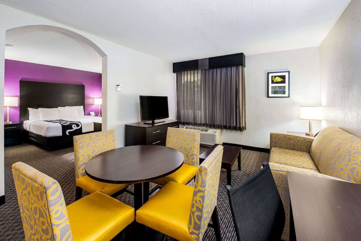 Une chambre d’hôtel avec un lit, une télévision, une table à manger avec des chaises jaunes et un canapé.