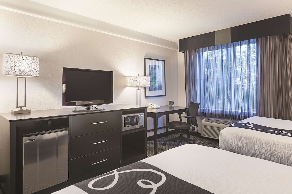 Une chambre d’hôtel équipée d’un lit, d’un bureau, d’une télévision, d’un réfrigérateur et d’une fenêtre avec des rideaux.