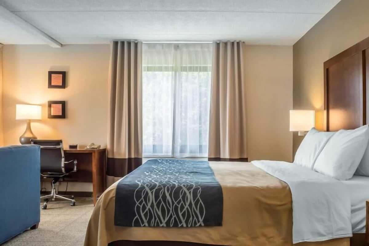 A hotel room with a bed, desk, chair, and two lamps.