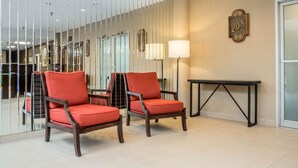 Un vestíbulo con dos sillones rojos acolchados, una mesa negra, una lámpara de pared y un cartel con un número.