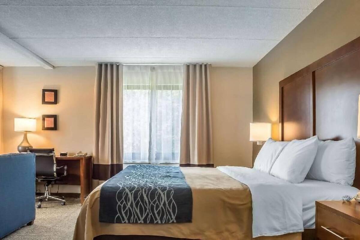 A hotel room with a bed, desk, chair, and curtains.
