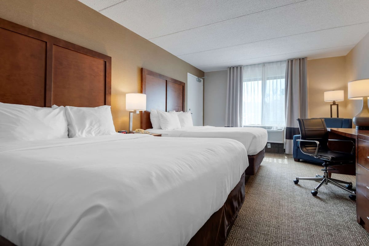 A hotel room with two beds, a desk with a chair, and a large window with curtains.