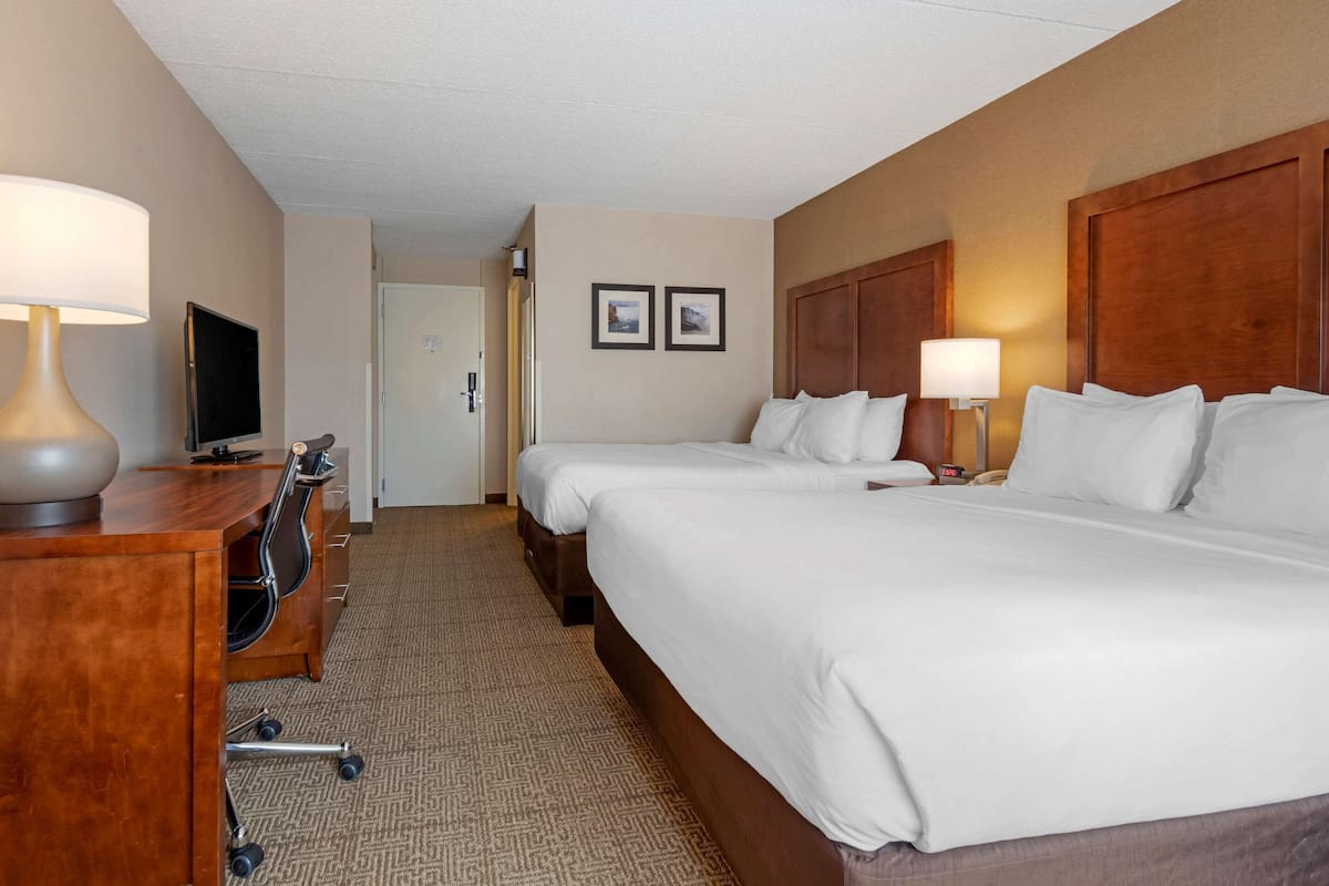 A hotel room with two beds, a desk with a lamp, a television, and a door leading to another room.