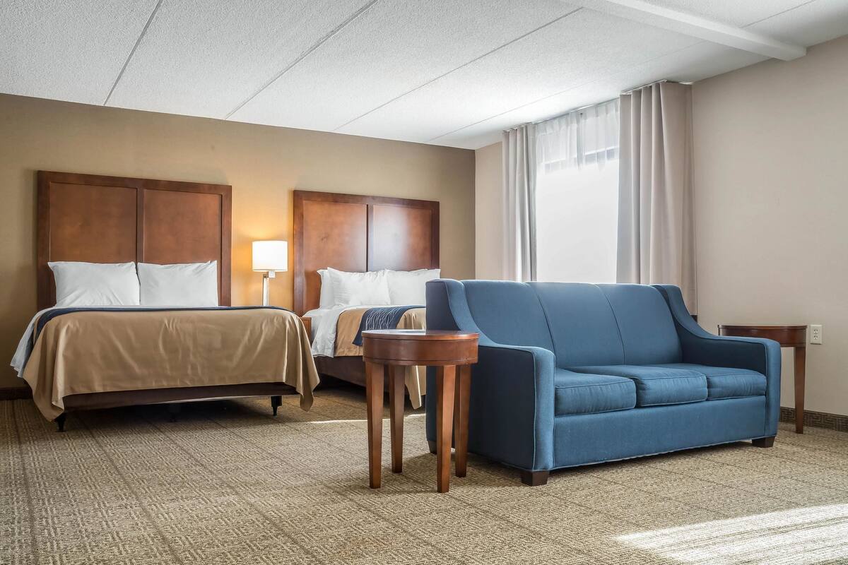 A hotel room with two beds, a blue sofa, a small wooden table, and a lamp.